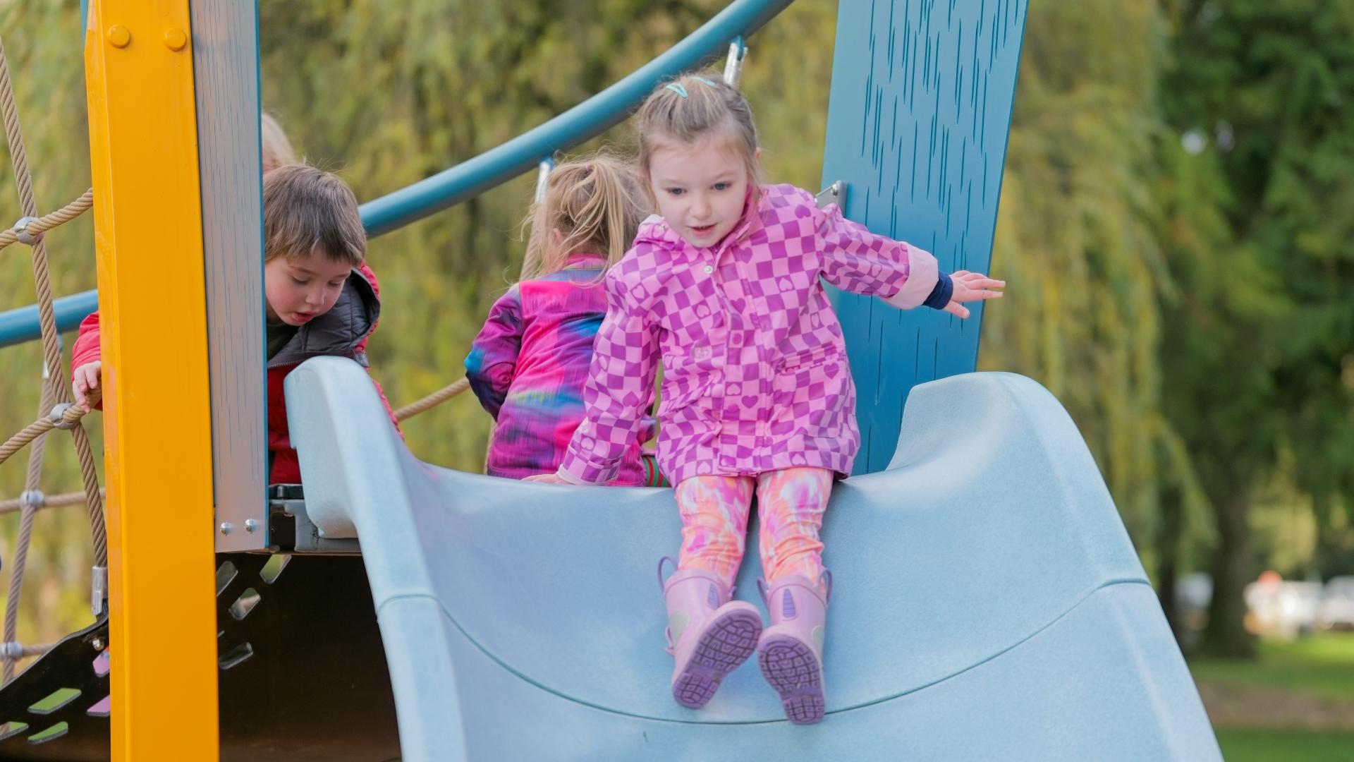 Small girl in pink raincoat at the top of an accessible slide