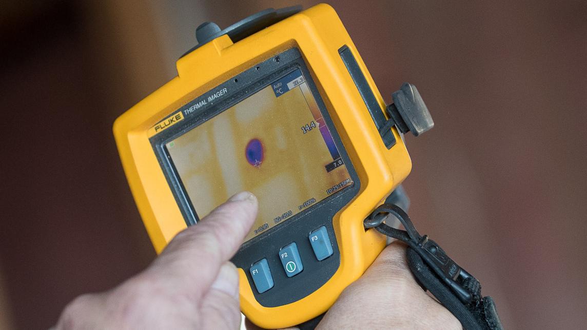 A worker points to a dark spot on a thermal imaging device at a house construction site.