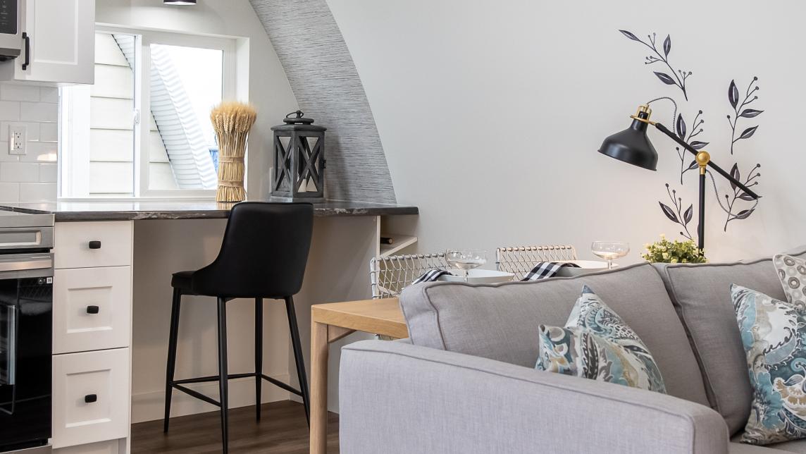 A stylish grey couch sits in front of a small kitchenette.