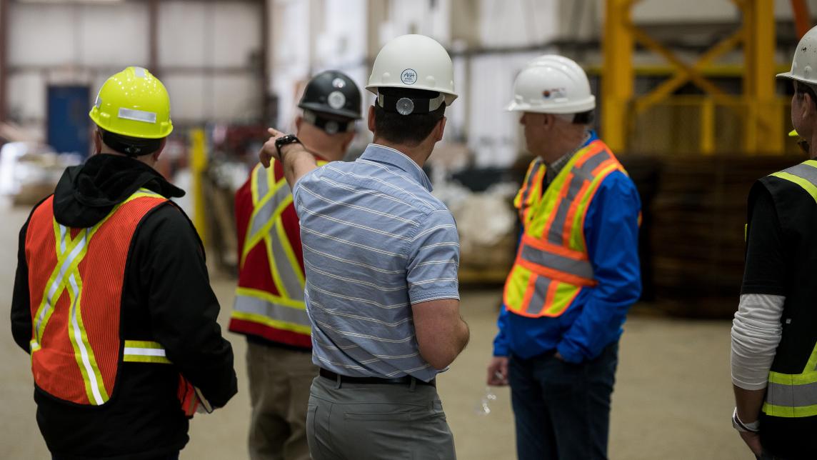 A man wearing a hard hat directs other men's attention towards one side of a wearhouse.