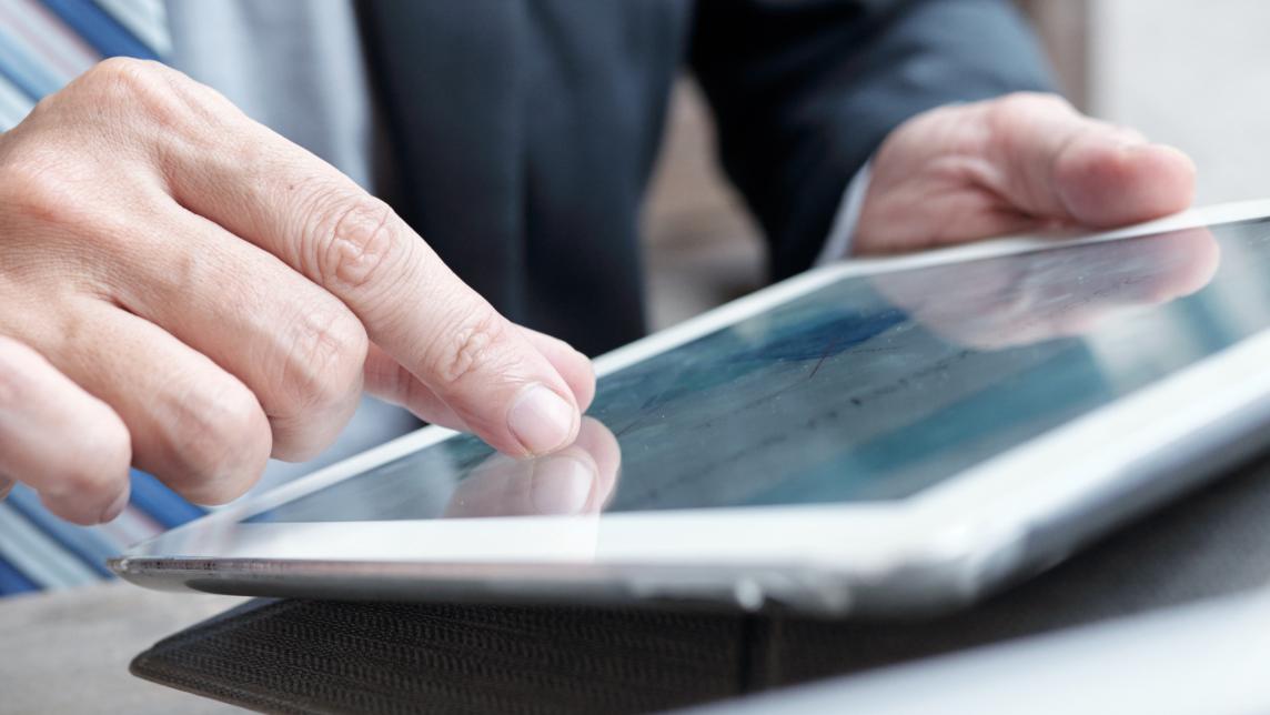 A man in a suit uses a pinch gesture to zoom in on his tablet screen.