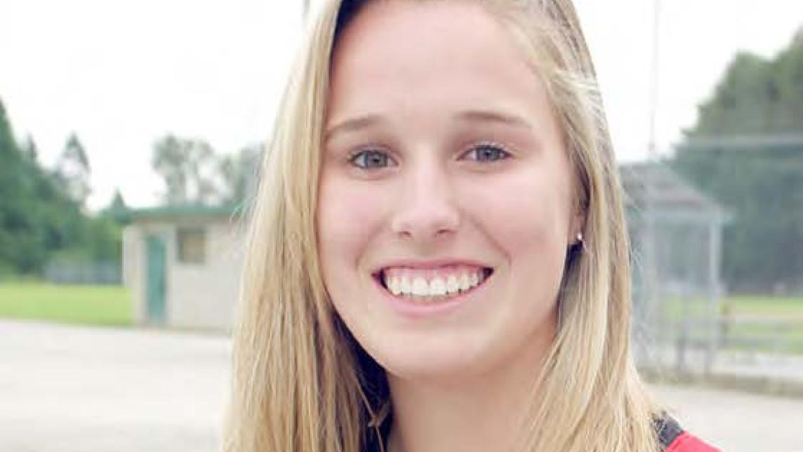 Larissa Franklin smiles as she stands in an empty baseball diamond wearing a baseball glove.