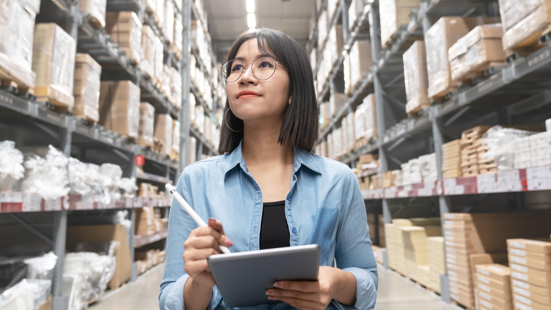 A woman with a tablet surveys the shelves in a warehouse, taking inventory.