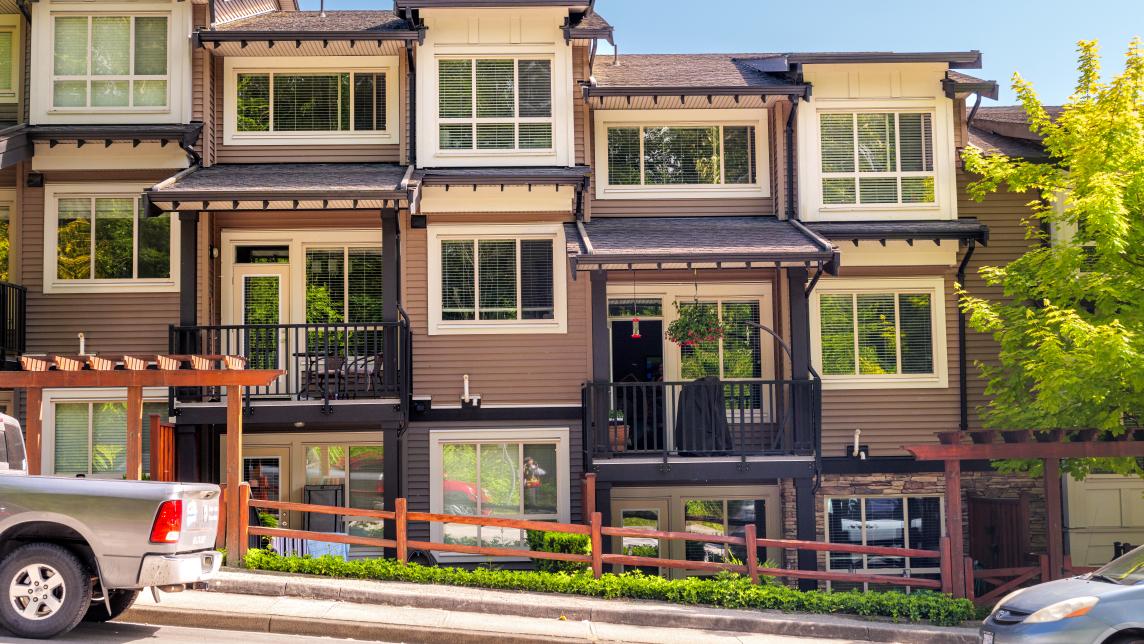 Brown townhouse housed in a single building next to a highly sloped street.