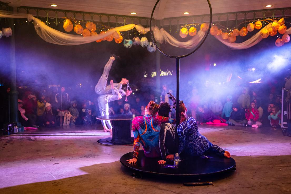 A crowd watches a set of performers as some perform a lift, and others wait their turn.