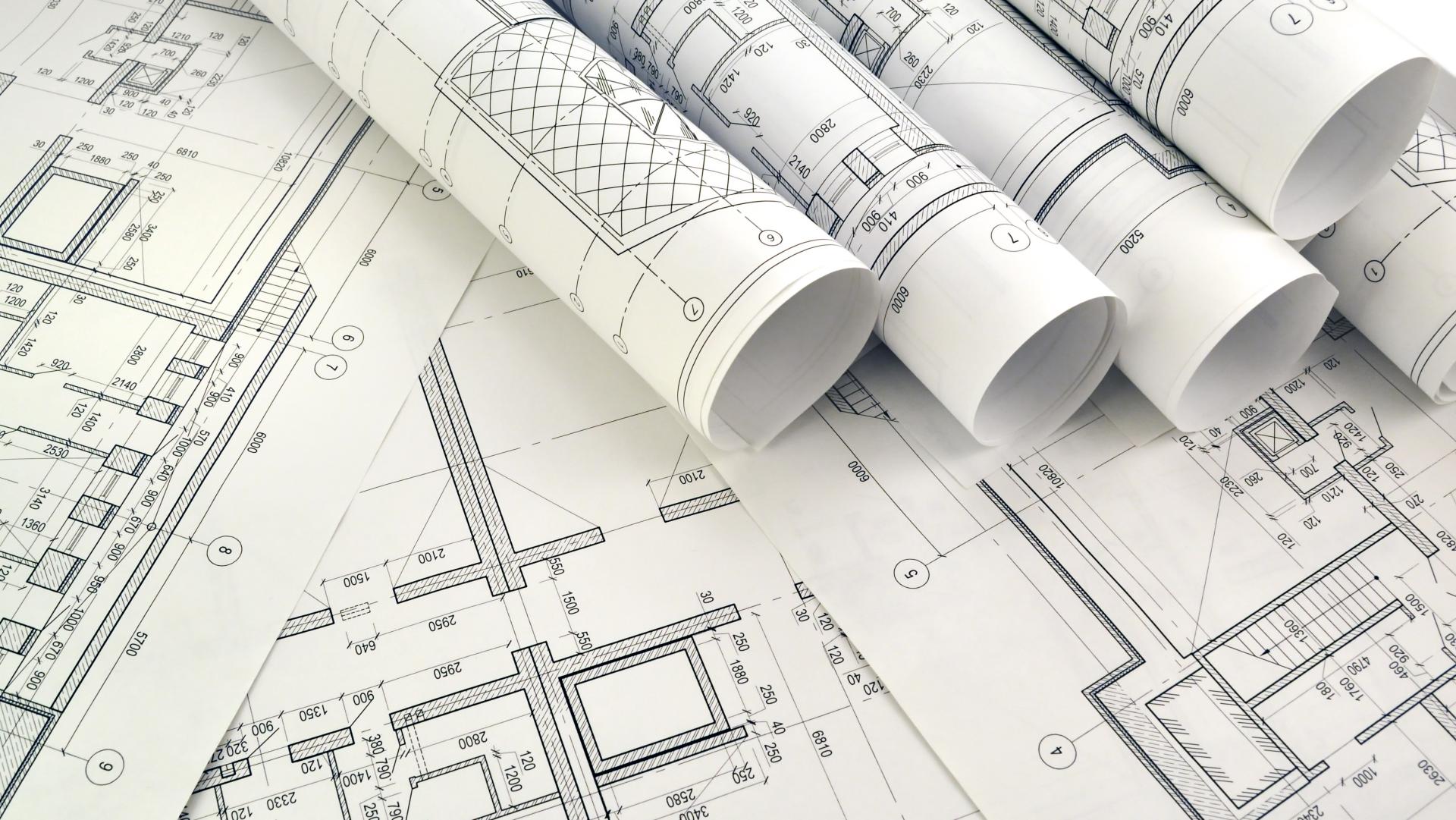 Rolled up white paper building plans sit on top of other flat plans.