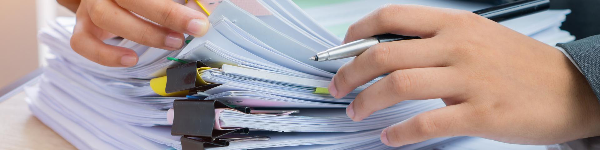 A person rifles through a large stack of binder-clipped paper packages.