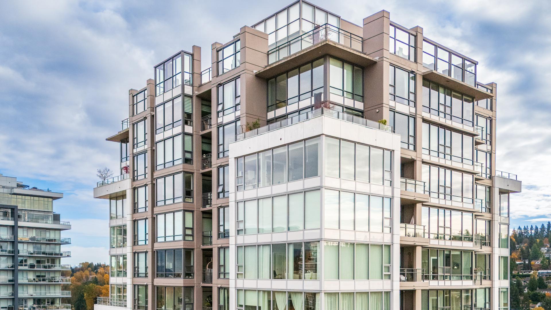 The sky reflects off the glass windows of a high-rise apartment building.