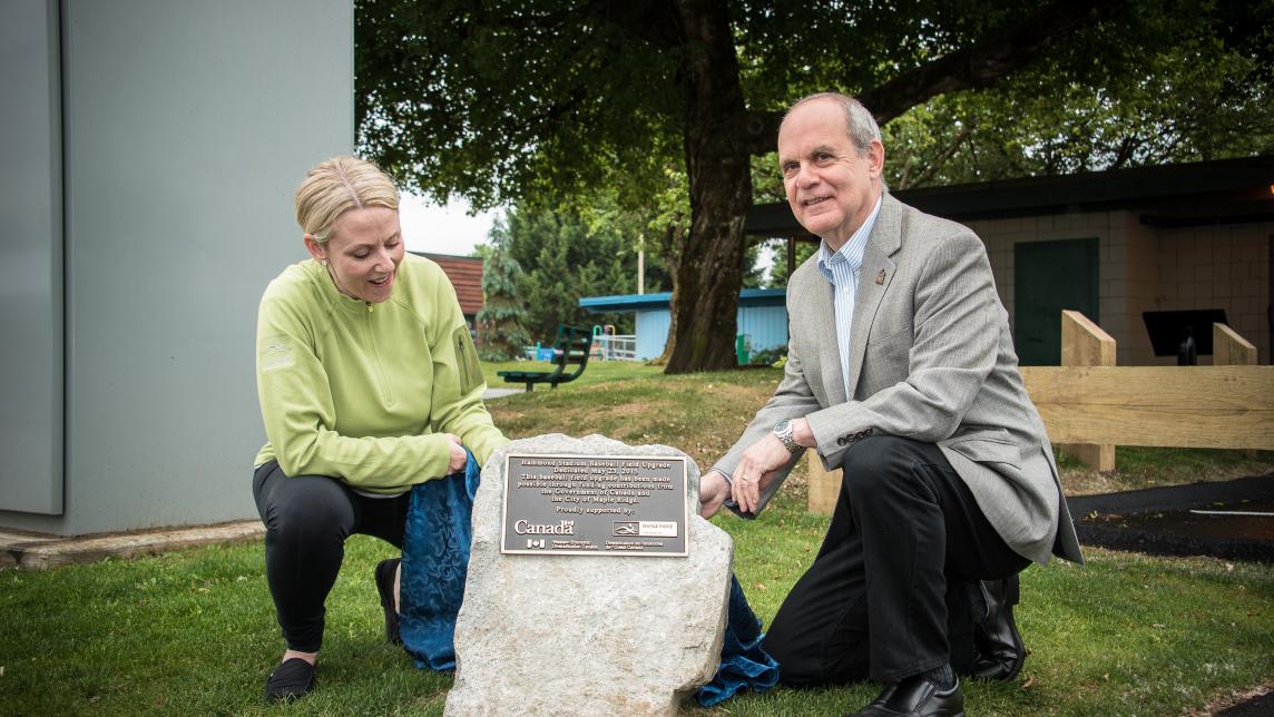 Two people squat down beside a dedication plaque that has been affixed to a rock at Hammond Field.
