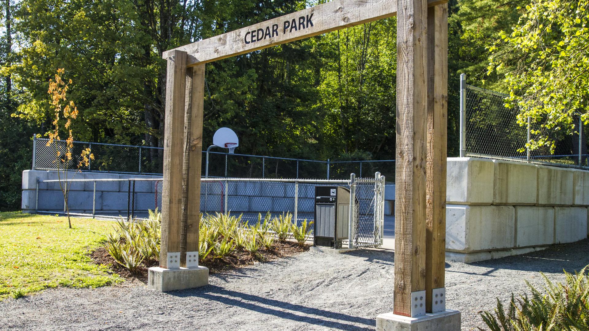 A large wood arch over a gravel pathway. Past the archway there is a fenced in court.