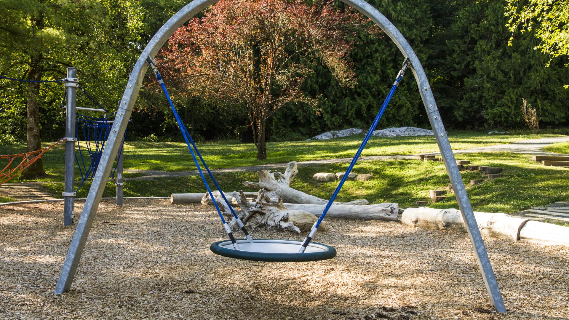 A large round swing under a metal archway on the playground mulch.