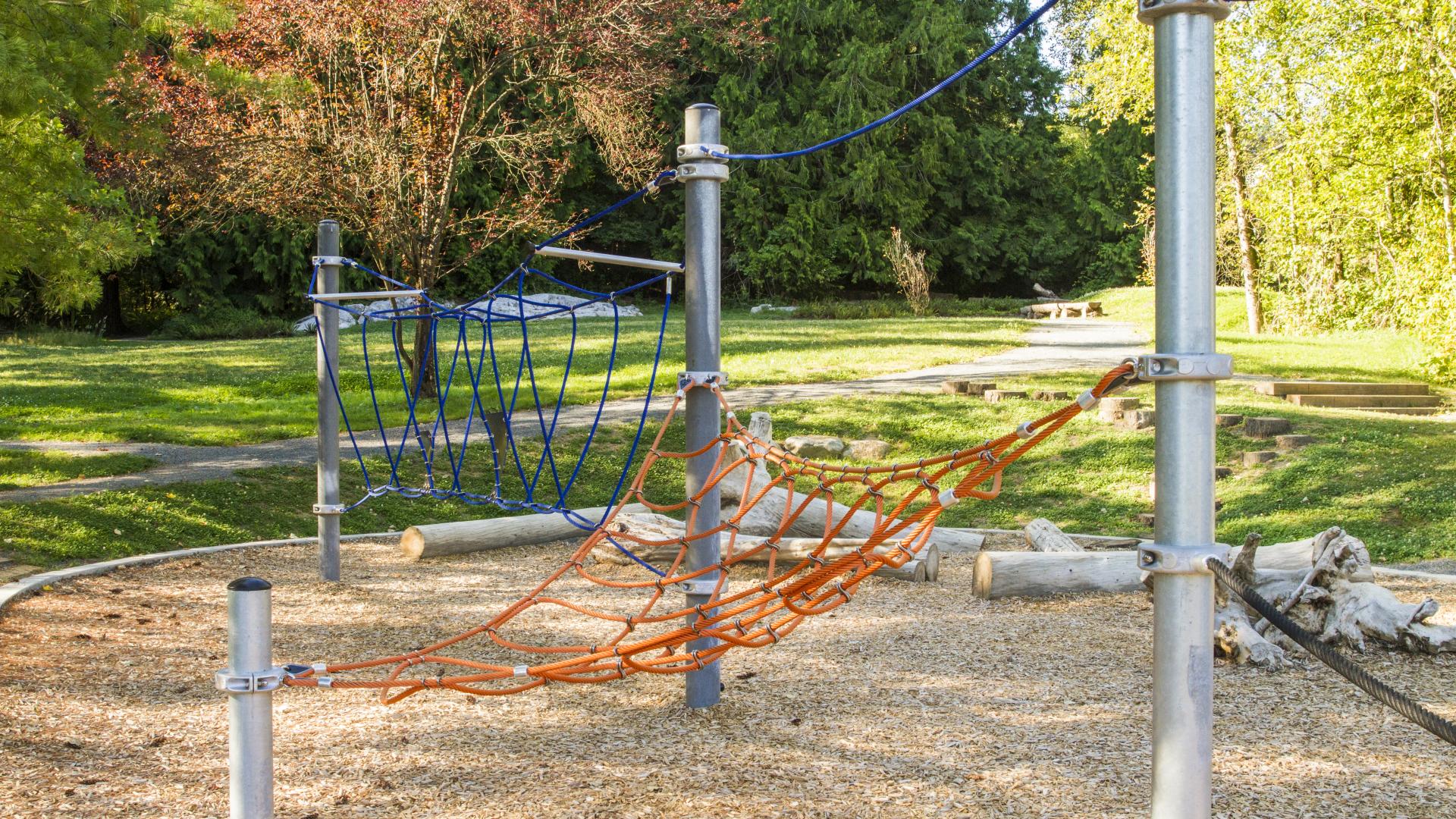 A rope net suspend between three metal posts for climbing on the playground.