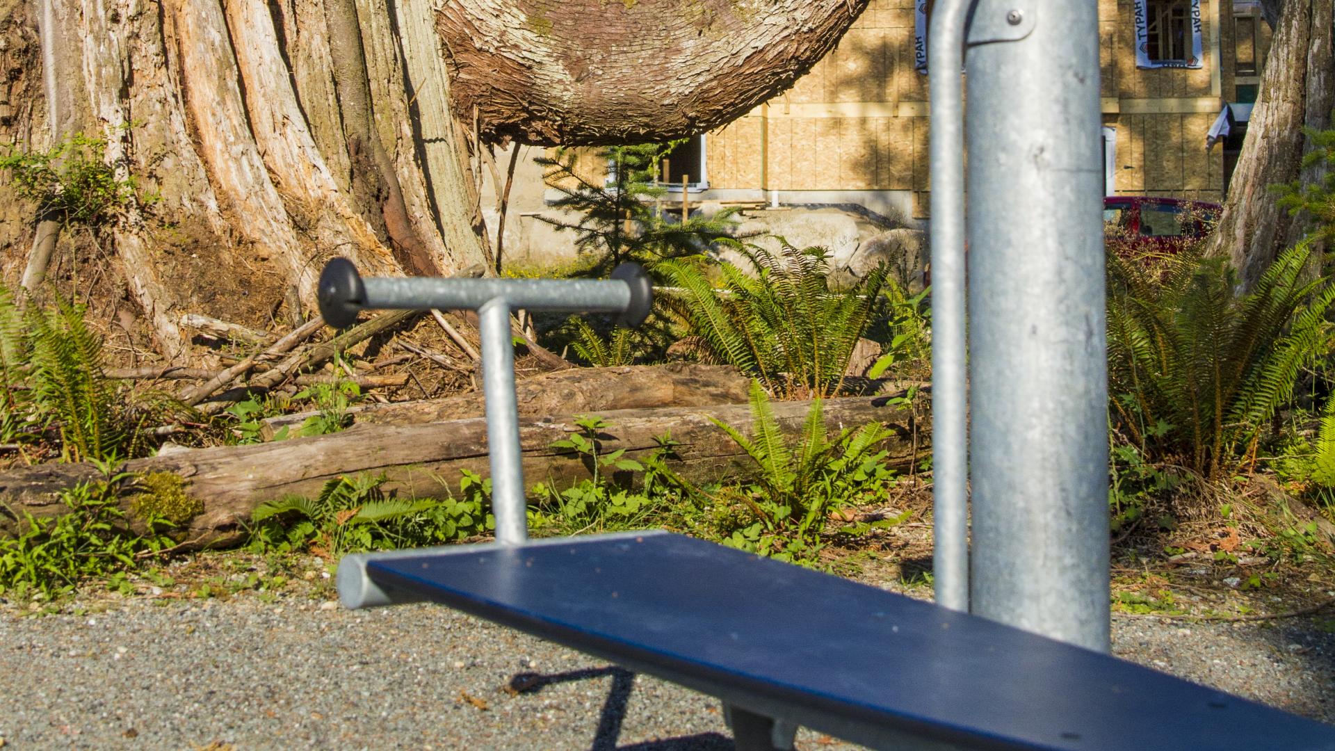 A piece of park gym equipment with a flat bench and a t-bar on one side.