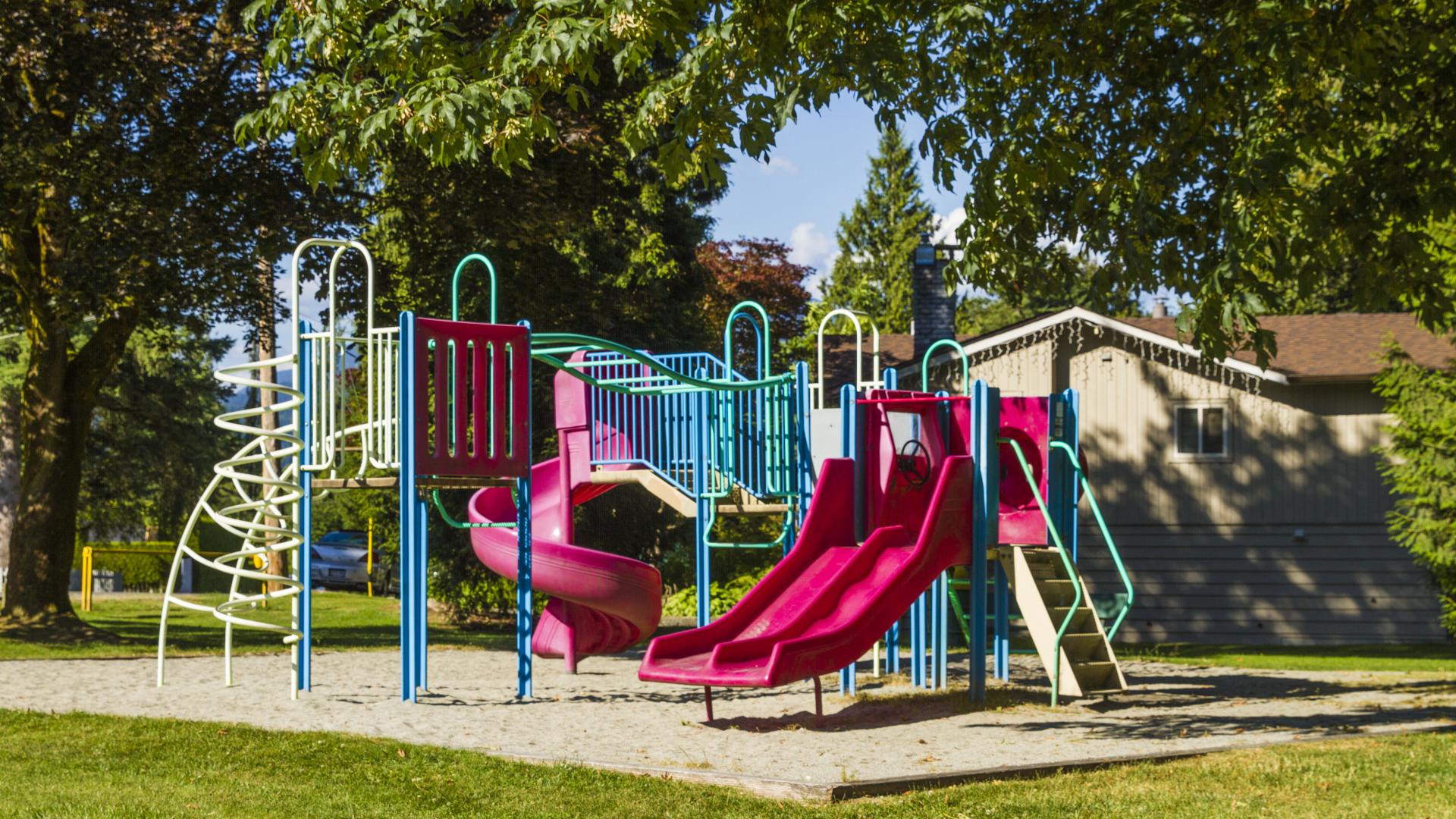 A colourful playground in a small sandbox, backing on to a houses backyard.