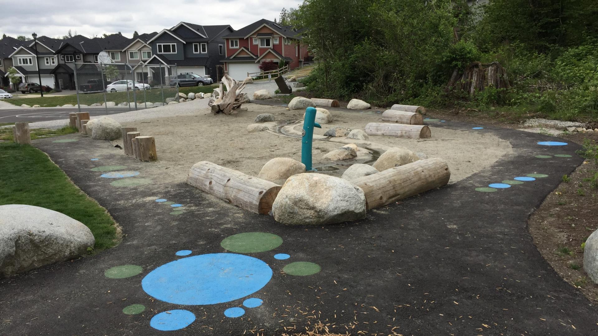 Sand play area with water pump and boulders and logs surrounding