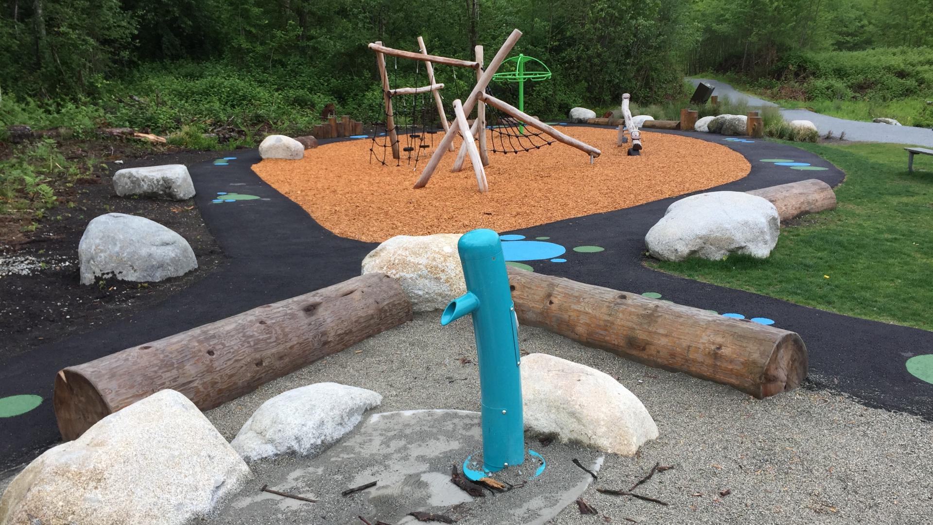 Water pump in sand play area with wood playground in the background