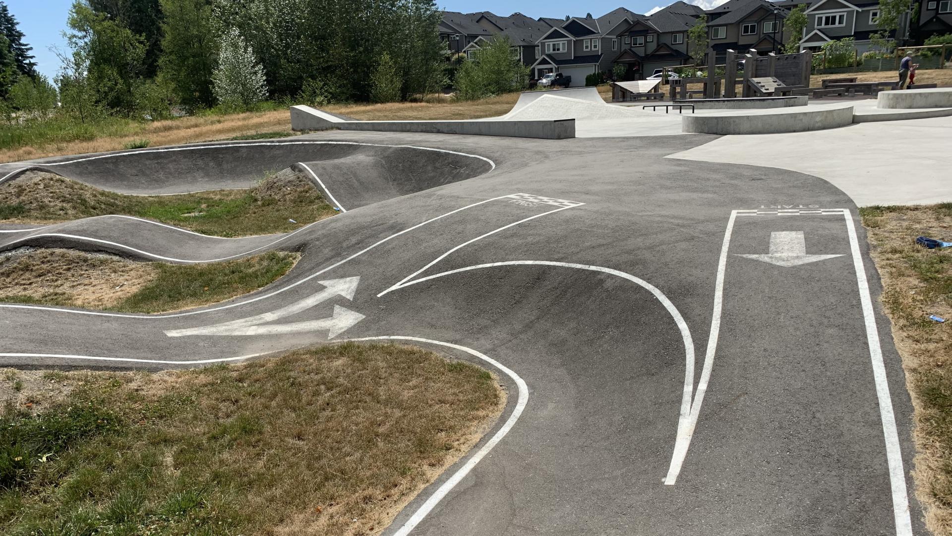 Pump track with directional arrows and skate park behind