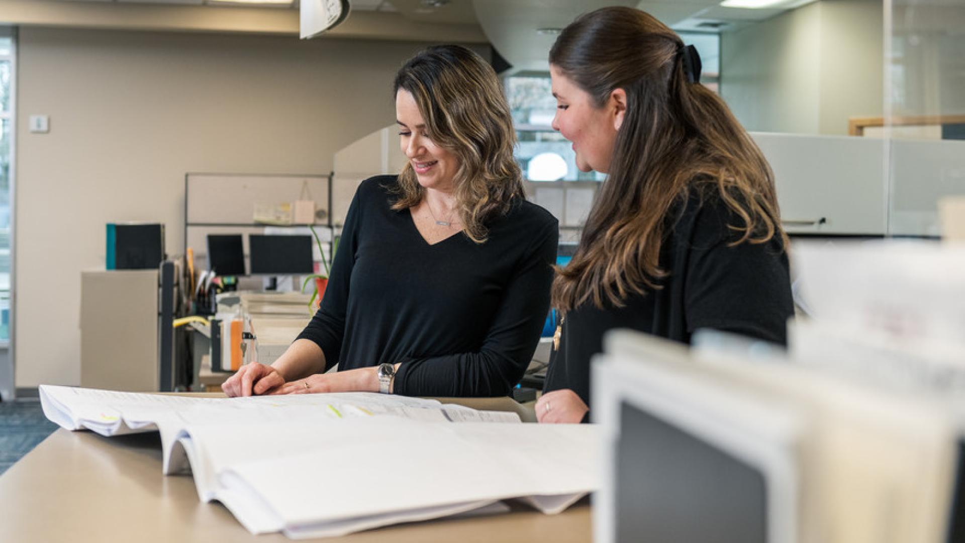 Two city staff survey large unfolded papers, evaluating the contents held within.