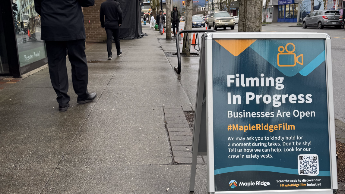 A signboard on 224th Street displaying the text "Filming in Progress - Businesses are Open"