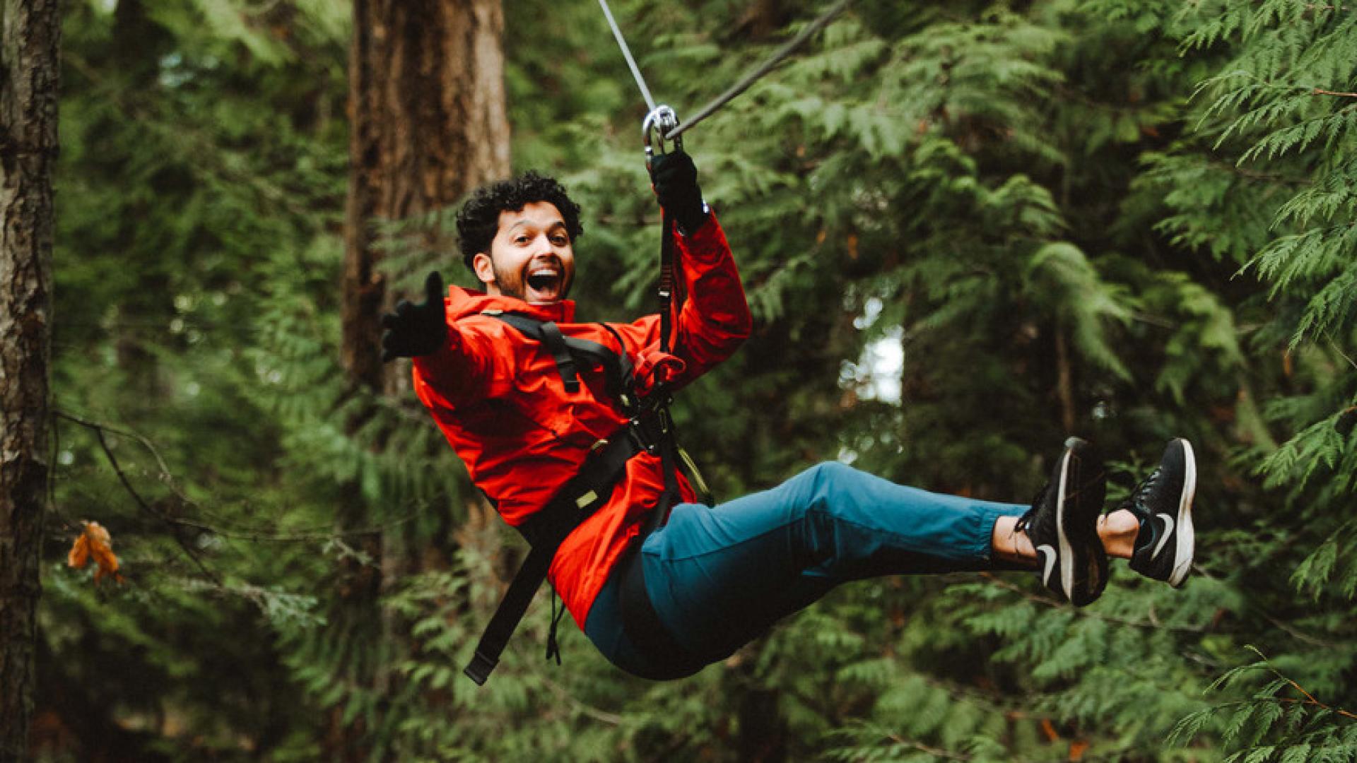 A young man reached out his hand as he zip lines through cedar trees.