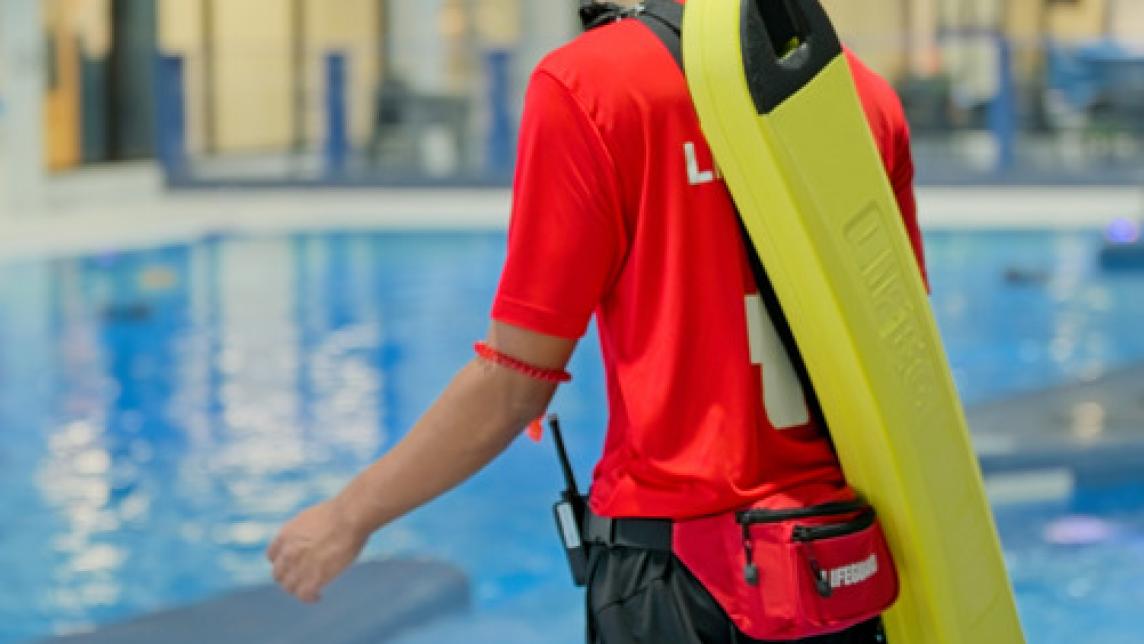 Image of lifeguard walking on the pool deck wearing a rescue tube