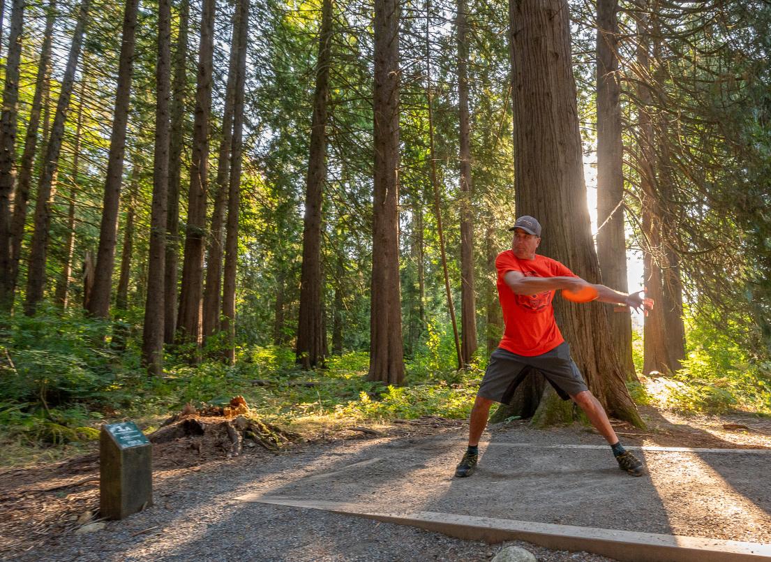 A man winds up to throw a frisbee for a game of disc golf surrounded by trees.