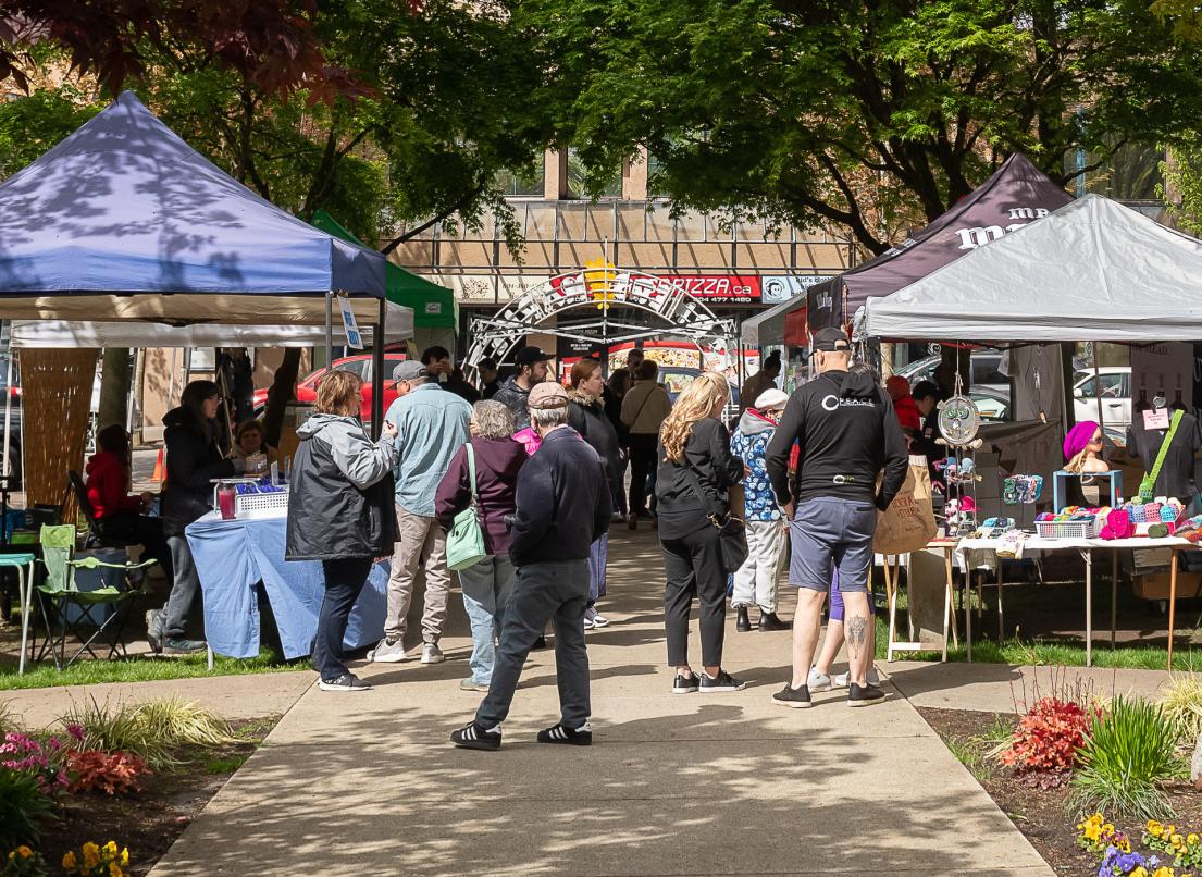 A crowd of people peruse the offerings at the Farmer's Market in Memorial Peace Park on a sunny day.