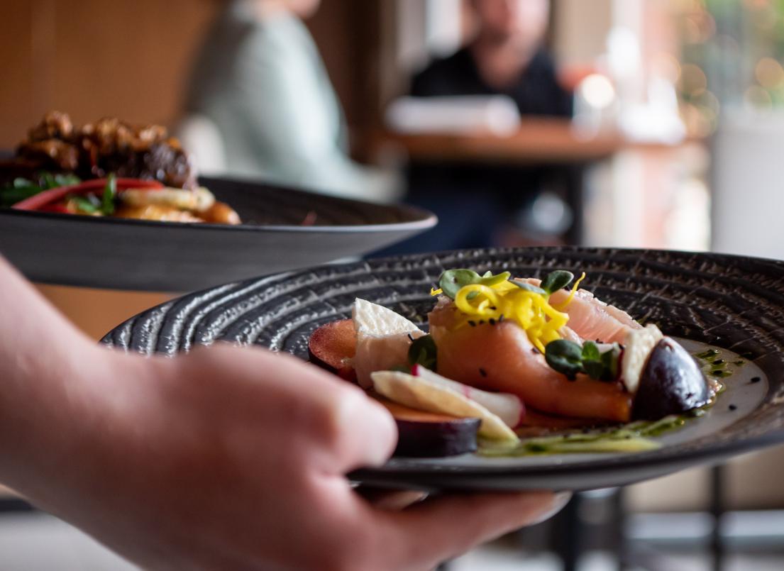 A waiter sets down two black plates, one has fish with vegetables while the other has beef.