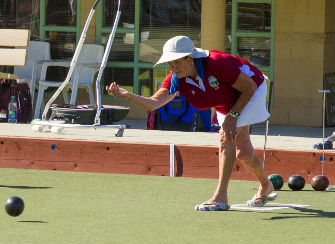 A woman lets go of a small lawn bowling ball on artificial turf.
