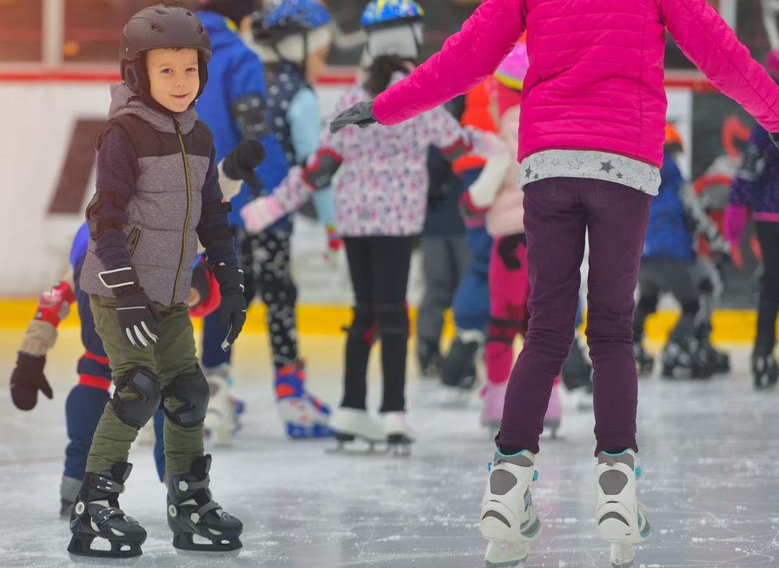 A young boy looks the opposite direction to the rest of his indoor ice skating class.