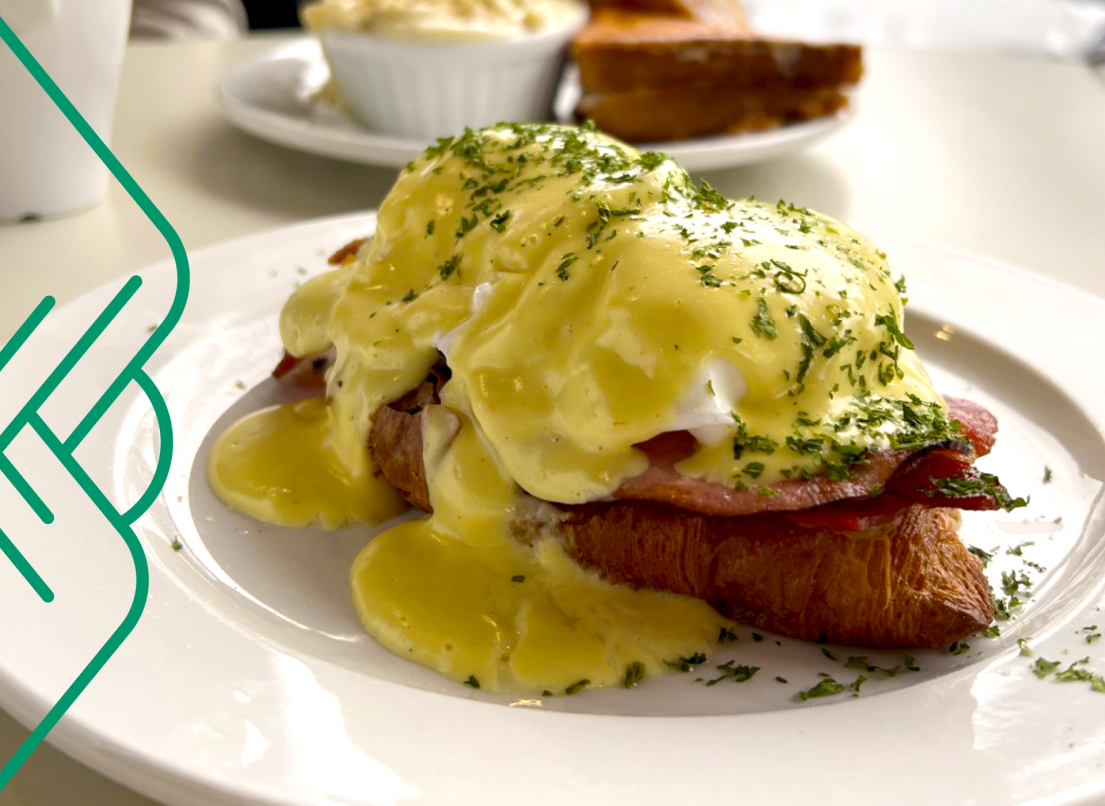 Rich hollandaise sauce cascades down the site of a plate of Eggs Benedict.