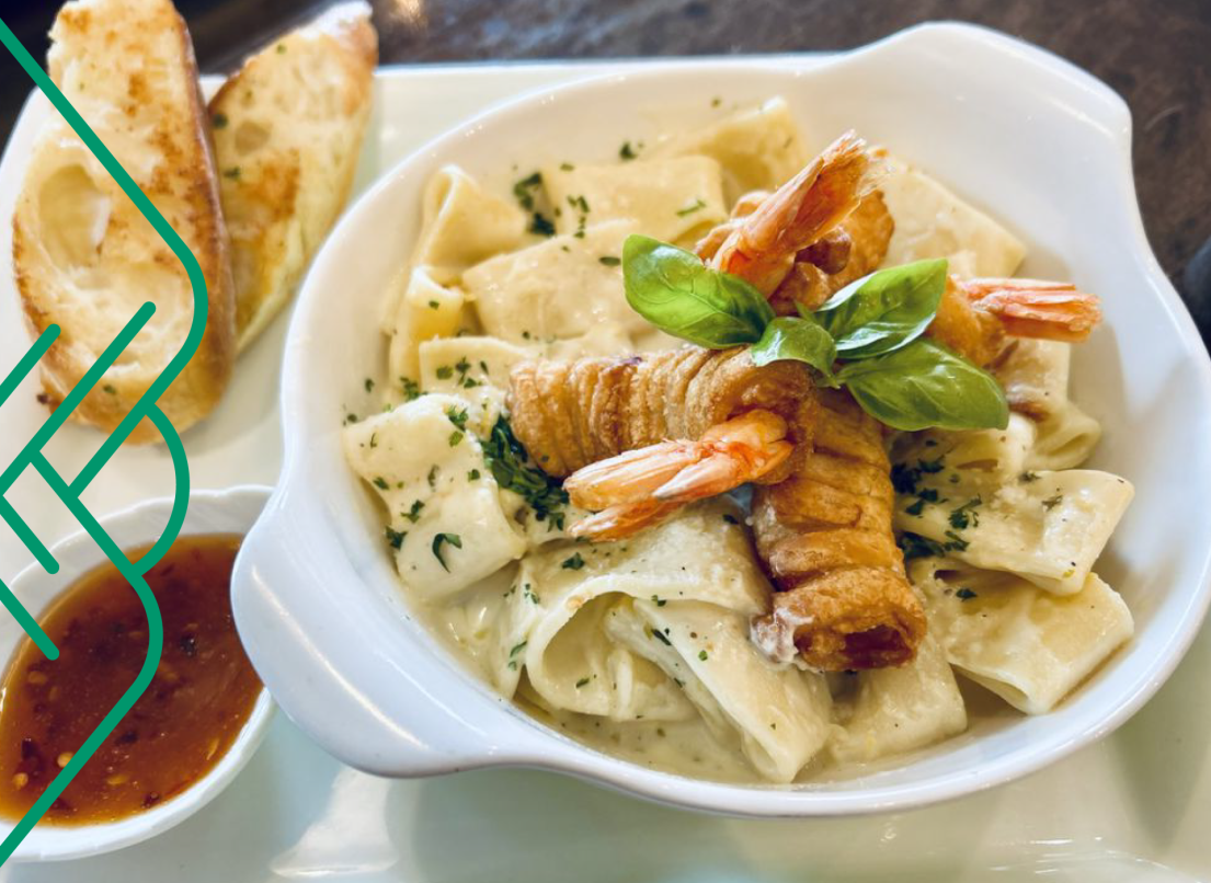 A seafood pasta sits in a small bowl next to a chilli sauce with toast on the side.