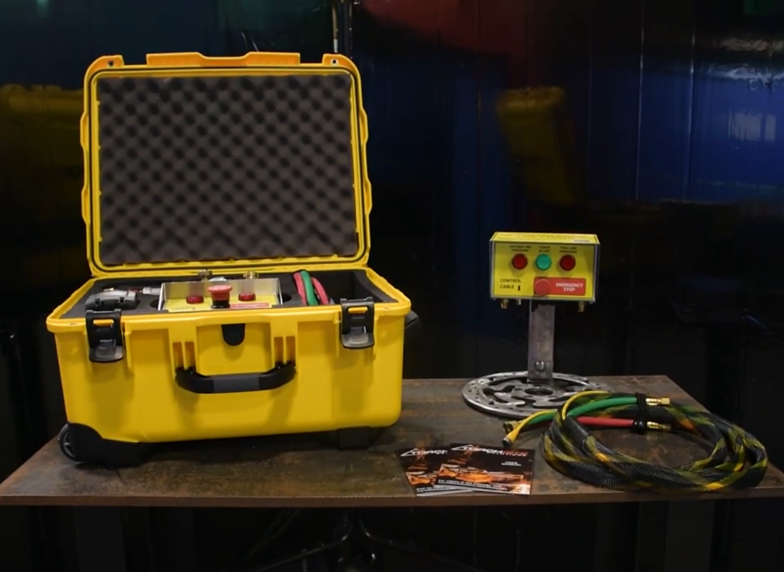 A yellow box and control panel with red and green lights and an emergency shut-off switch are displayed on a table.