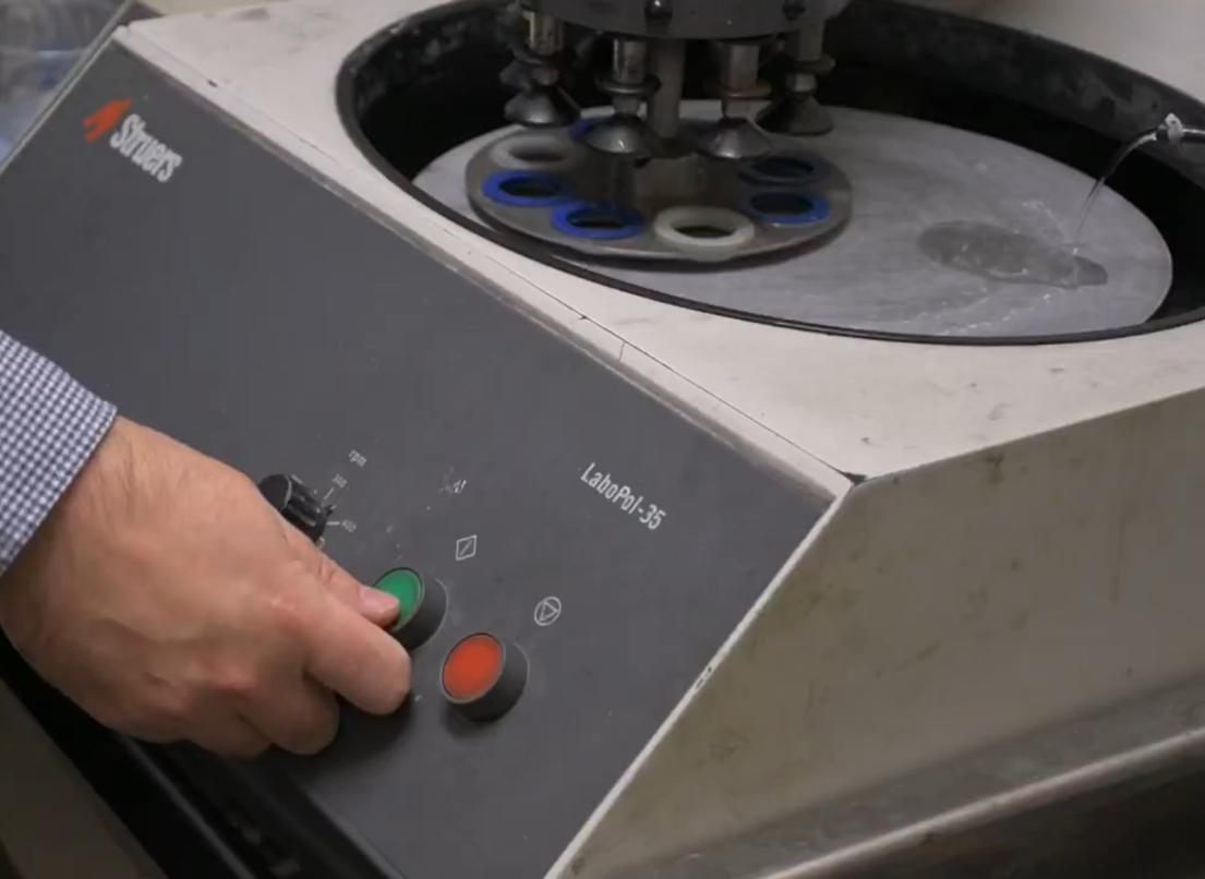 A worker presses a green button to turn on a centrifuge with clear liquid being poured on it.