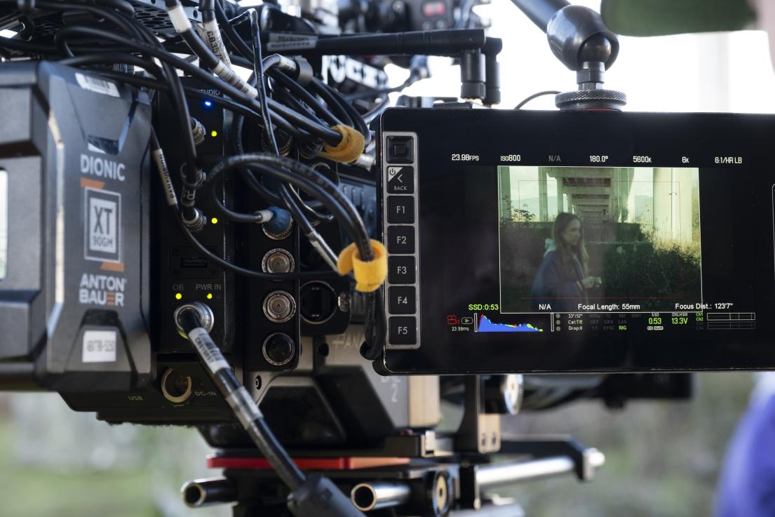 A film camera pointed at an actor standing underneath the Golden Ears Bridge.