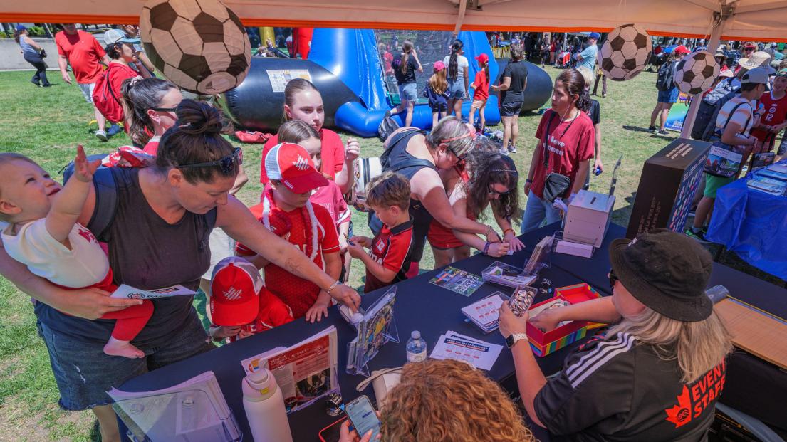 Part of the crowd gathers around a booth. A baby being held reaches for a soccer-ball shaped lantern.