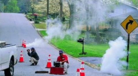 Workers observe fog exiting from maintenance holes and drains in a roadway
