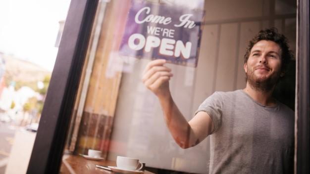 Smiling man hanging an Open sign in a shop window