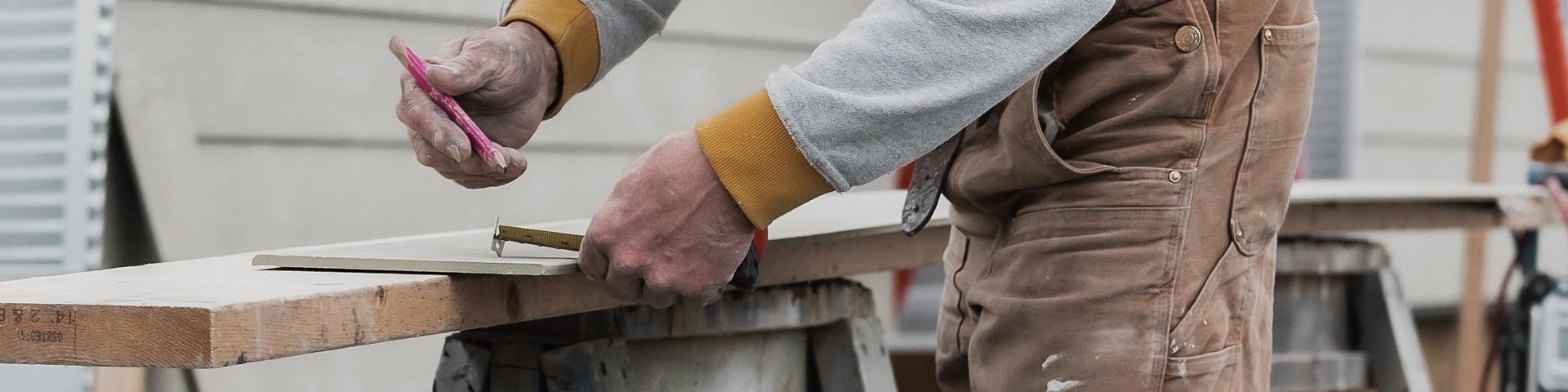 A carpenter makes a mark on a piece of plywood after measuring.