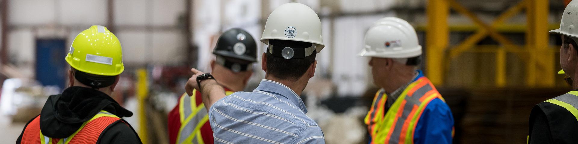 A man wearing a hard hat directs other men's attention towards one side of a wearhouse.
