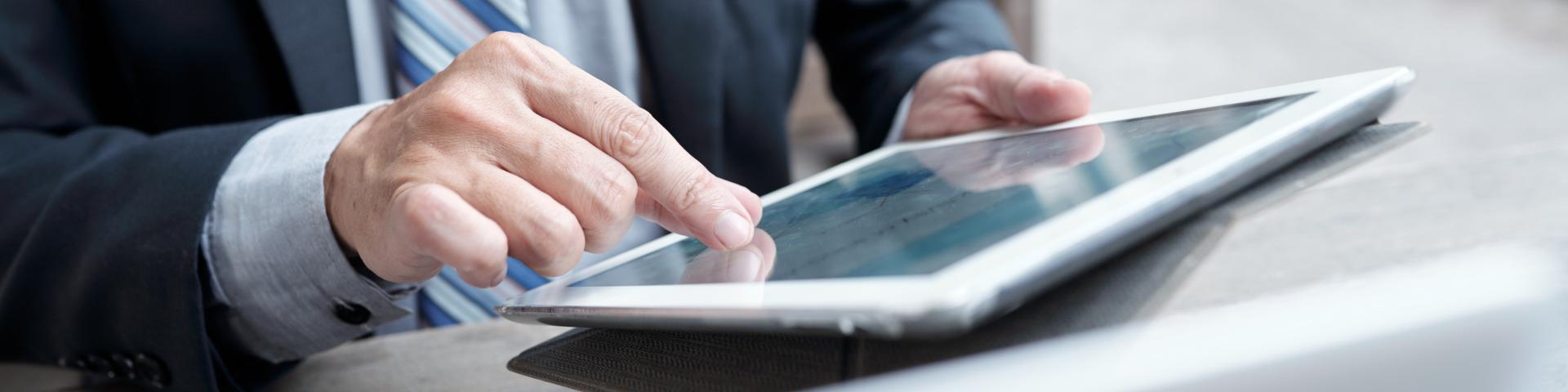 A man in a suit uses a pinch gesture to zoom in on his tablet screen.