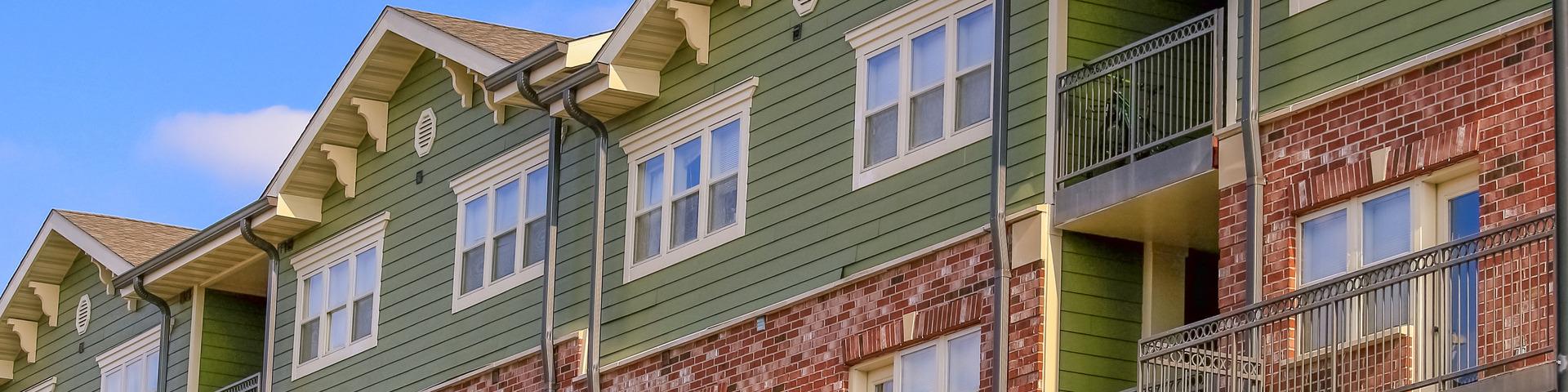 A brick building topped with green siding sits against a bright blue sky.