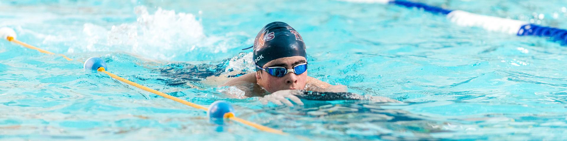 A boy wearing a swim cap and googles kicks down a designated swim lane at a pool.