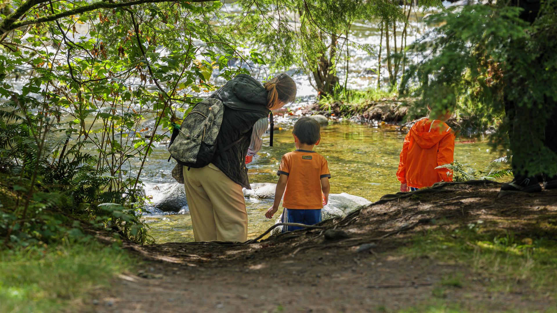 A woman bends over to point something out to one of two boys with her at the riverfront.