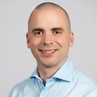 Even Moore smiles at the camera wearing a light blue collared shirt.